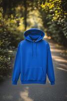 A vibrant blue color hoodie mockup against a blurred natural background, featuring a front pocket and drawstrings. Sweatshirt with hood long sleeve for print. photo