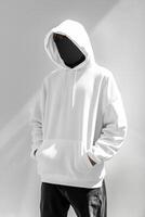 A man in a white hoodie standing in front of a white wall photo