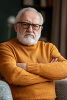 An older man with glasses and a beard sitting on a couch photo