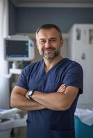 A confident male healthcare professional in scrubs, smiling with arms crossed in a medical setting. The background features medical equipment and a bright, clean environment. photo
