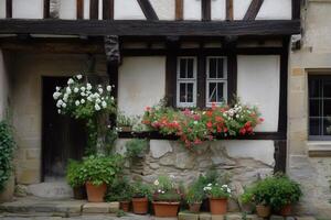 A charming old Tudor style house with a wooden frame, featuring a stone wall and vibrant flower pots. The window boxes are filled with colorful flowers, creating a picturesque scene. photo