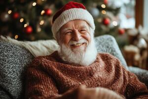A smiling old man wearing a santa hat sitting on a couch photo