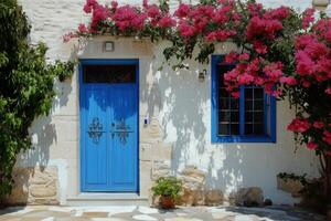 A charming white Mediterranean house with a vibrant blue door and window, adorned with blooming pink bougainvillea. The entrance features decorative ironwork and a small potted plant. photo