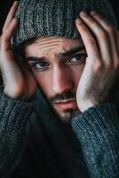 A man in a sweater and hat is holding his head photo