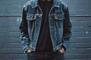 A man wearing a denim jacket standing against a brick wall photo