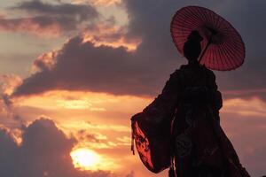 A silhouette of a person holding a red parasol against a vibrant sunset sky with clouds. The figure is dressed in traditional attire, creating a striking contrast with the colorful background. photo