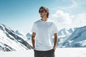 A man in a white t - shirt standing on a snowy mountain photo