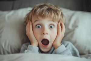A young boy is looking surprised in bed photo