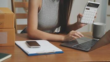 A woman is sitting at a desk with a calculator and laptop video