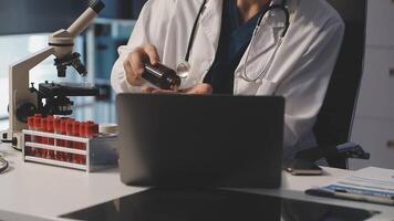 A doctor is working on a laptop and looking at a microscope video