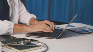 A man in a white coat is typing on a laptop video
