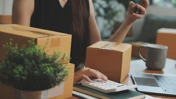 A woman is using her laptop while sitting at a desk with boxes and a plant video