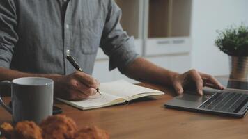 Man writing on notebook at desk with laptop video