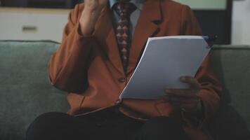 A man in a suit and tie sitting on a couch with a notepad video
