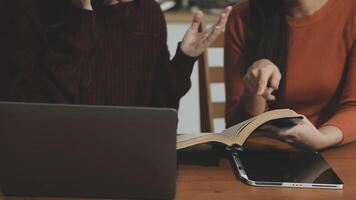 Two women sitting at a table with a laptop and an open book video