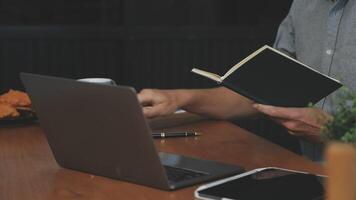 A man is sitting at a table with a laptop and a book video