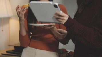 Two women standing in front of a table holding a tablet video