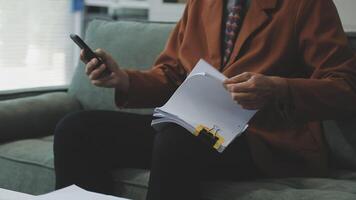 A man in an orange jacket is sitting on a couch holding a phone and a piece of paper video
