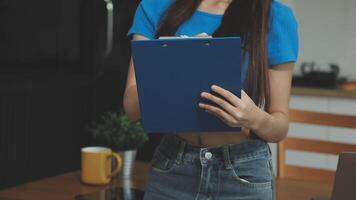 A woman holding a clipboard while standing in front of a laptop video