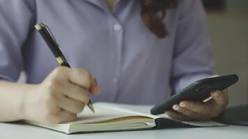 Woman writing in notebook and using smartphone video