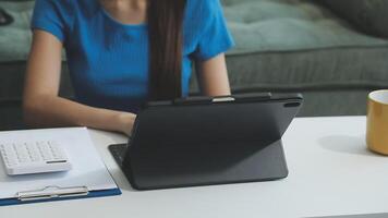 A woman sits at a desk with a tablet and a calculator video