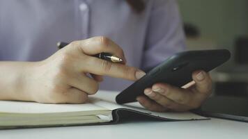 A person is using a cell phone while writing in a notebook video