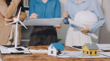 Three people standing around a table with a house and wind turbine video
