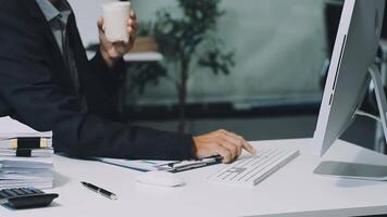 A man in a suit sitting at a desk with a computer and a cup of coffee video
