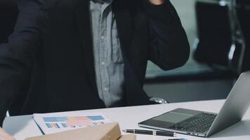 A man in a suit is talking on the phone while sitting at a desk with a laptop video