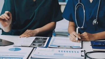Two doctors sitting at a table with papers and a laptop video