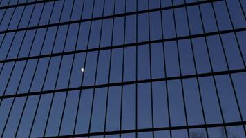 The moon is visible through a grid or fence, creating a boundary effect against the evening sky video