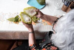 A senior mexican woman is showing the inside of a fresh cooked chayote after peeling it photo