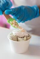 A worker is decorating a rolled ice cream tub with yogurt bubble toppings with a spoon photo