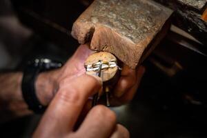 Jeweler hands setting a diamond into a ring with a burin in a jewelry workshop. Goldsmith working and creating a gold jewel. photo