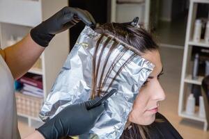 Hairdresser hands separating woman hair with aluminium foil photo