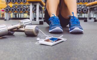 Sporty man sitting with dumbbells and smartphone in gym floor photo