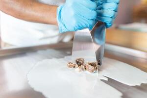 A worker is using spatulas to chop chocolate and mix it with milk on a rolled ice cream machine photo