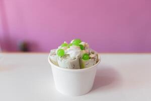 Close up of a rolled ice cream decorated with green bubbles and yogurt toppings photo