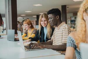 Cheerful diverse friends doing assignment using laptops in university photo