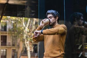 Man drinking takeaway coffee and checking wristwatch in city photo