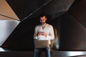 Man with laptop browsing smartphone in studio photo