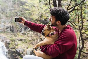 Smiling traveling man taking selfie with dog in forest photo