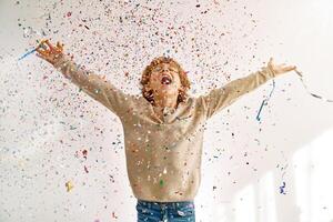 Happy boy enjoying falling confetti and sparkles and shouting jo photo