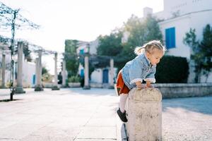 Little girl climbs a stone fence in the courtyard of the house photo