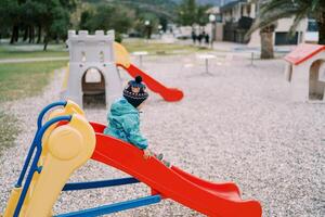 Little girl slides down a colorful slide in the playground. Side view photo