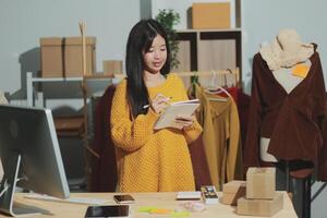 Asian woman writing on paper while standing in front of clothes photo