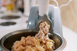 Electric meat grinder twists minced meat into a pan on the table photo