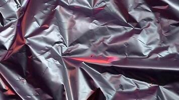 Holographic Foil Loop Futuristic Chrome Texture Animation. A close-up photograph of a shiny, metallic surface with a crumpled texture, reflecting light and creating a dynamic, almost abstract pattern video