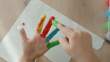 A 4-5-year-old child's open palm with fingers stained in different paint colors. Each finger is covered in a unique bright shade, creating a playful and artistic look. Top-view close-up shot video