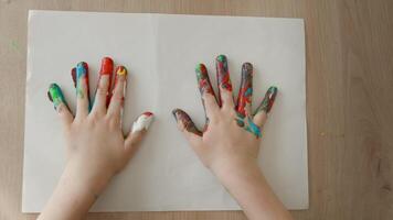 children palms stained with paint, a child makes an imprint of his palms on a piece of paper, open palm of a 4-5 year old child in top view video